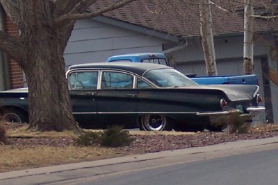 1972 Ford Ranchero - A black 1959 sedan with distinctive fins is parked next to a blue pickup truck.