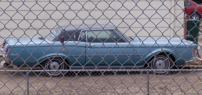 1972 Ford Ranchero - A side profile of a blue coupe with a black top is visible through a chain-link fence.