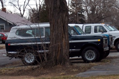 1972 Ford Ranchero - A dark blue and white SUV with a camper shell is parked next to a tree, with other vehicles behind it.