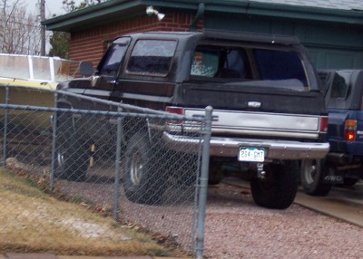 1972 Ford Ranchero - Black 1973 Chevrolet K5 Blazer with camper shell, parked next to a blue pickup truck.