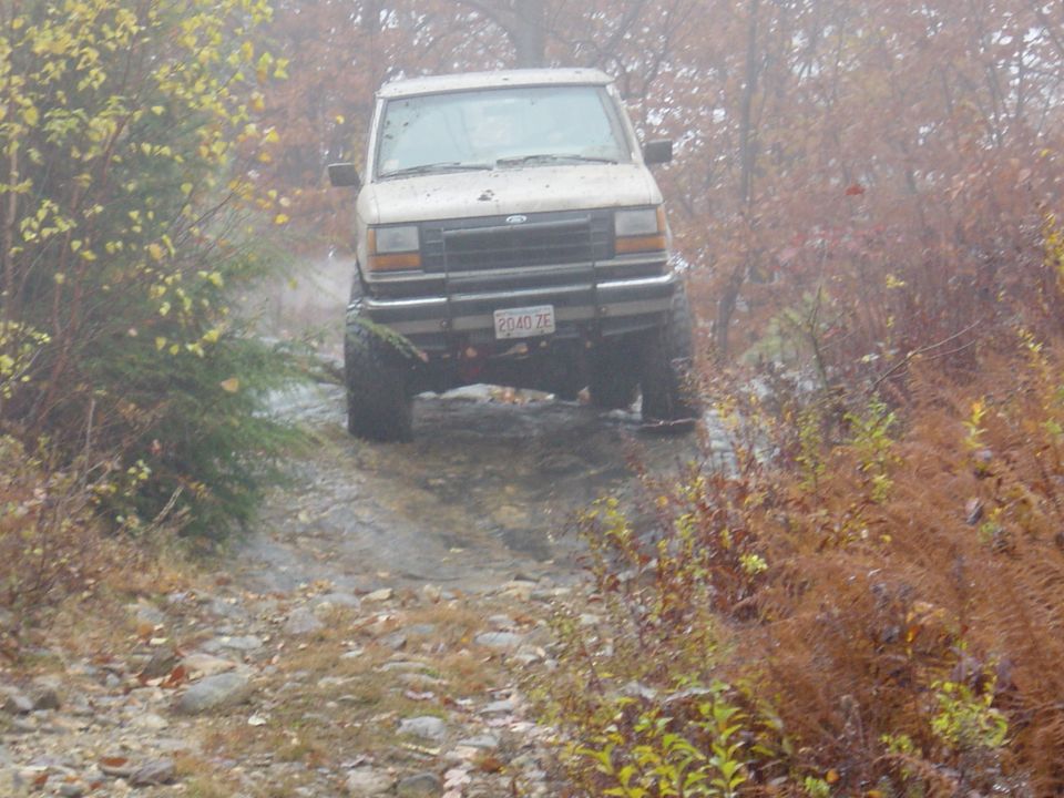 Lifted Ford pickup climbing rocky muddy trail head-on through foggy autumn woods
