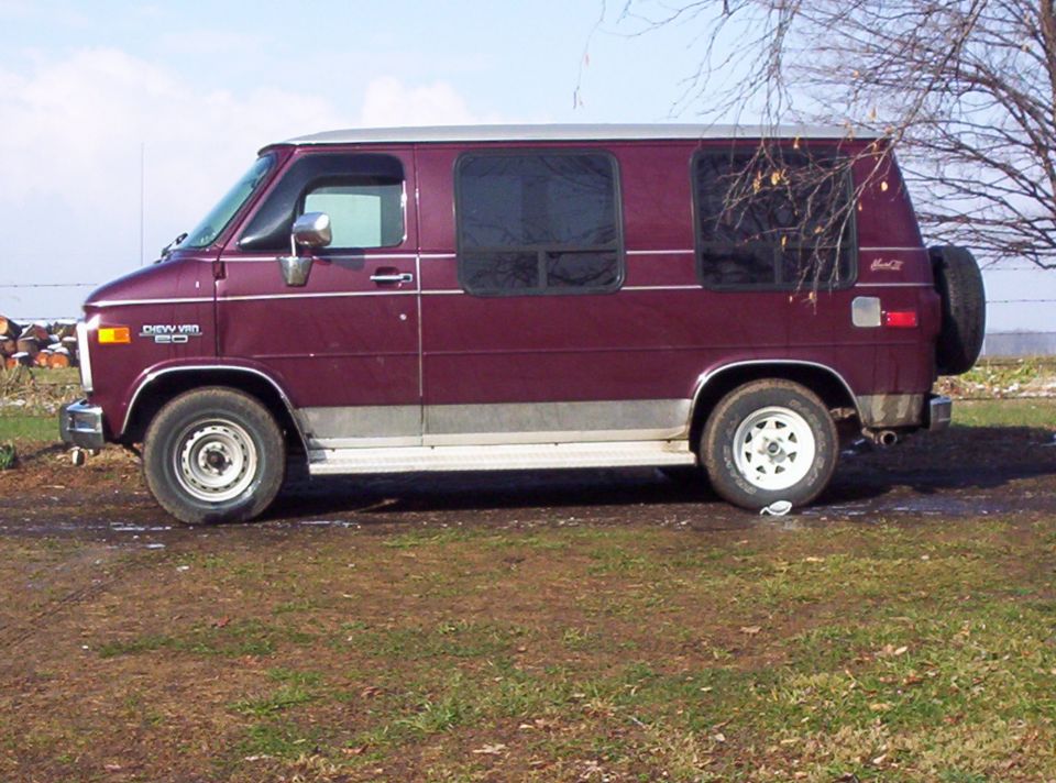 Maroon van with silver trim, spare tire on back. Has 'Chevy Van' badge