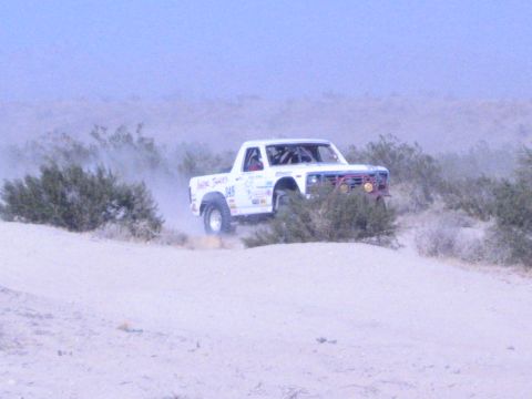 White number 949 off-road race truck driving through desert brush