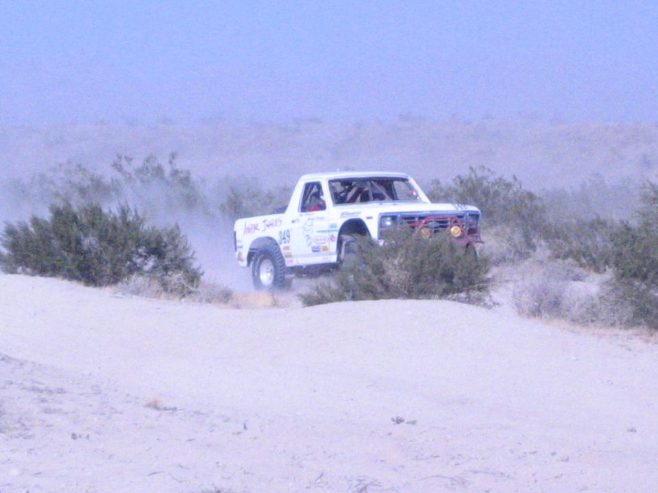 White number 949 off-road race truck driving through desert brush