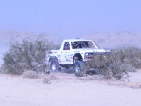 White 949 race truck driving among green desert bushes