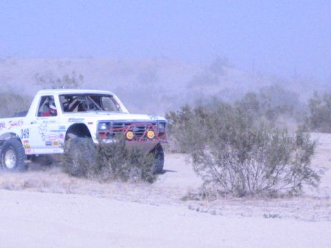 White 949 race truck with red brush guard and amber lights in desert