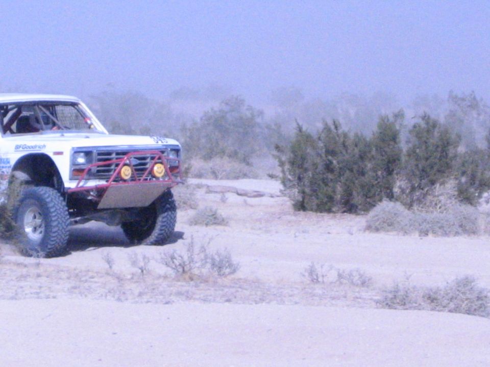 White race truck with red brush guard and amber lights among bushes