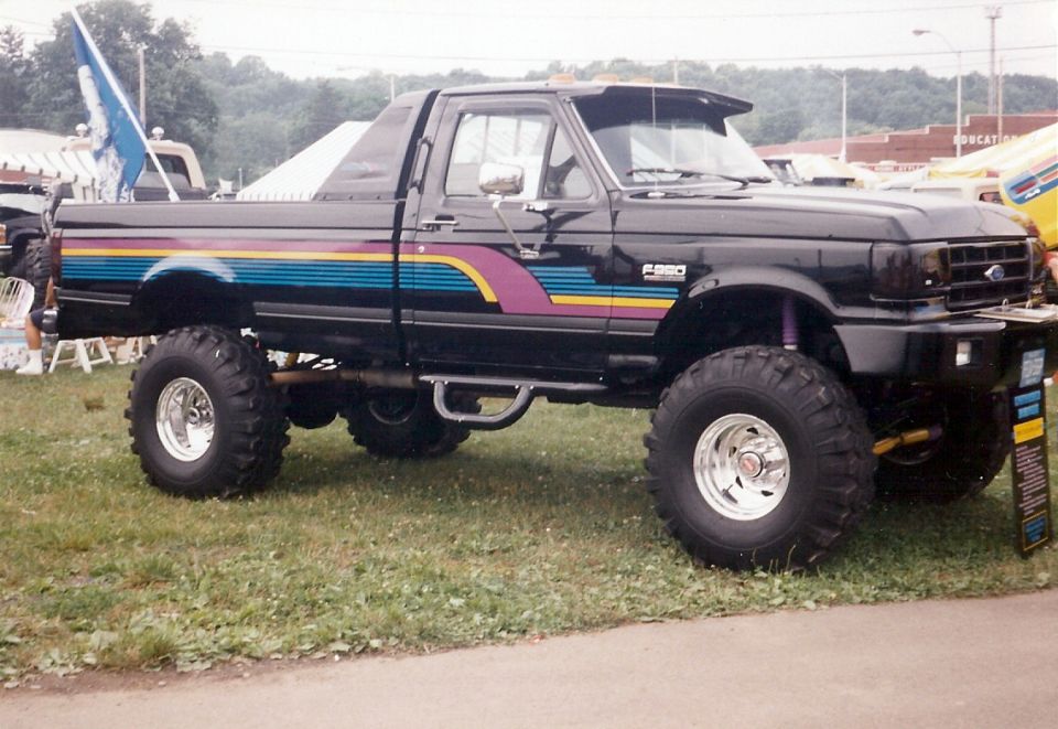Lifted black Ford F-350 pickup with purple and teal stripes and mud tires at an outdoor show