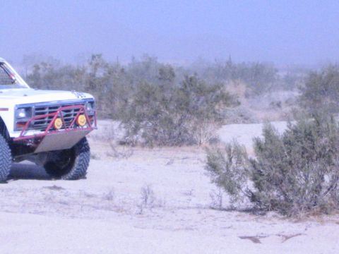 Front of white race truck with red brush guard parked in desert brush