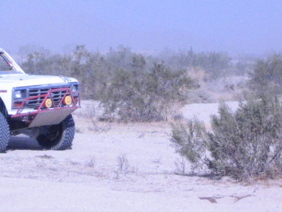 Front of white race truck with red brush guard parked in desert brush