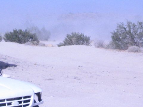 White truck hood at edge of frame on dusty desert flat with brush and haze