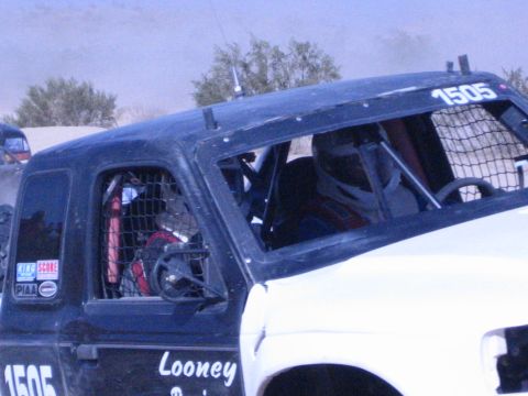 Dark off-road race truck number 1505 with caged windows, kicking up dust