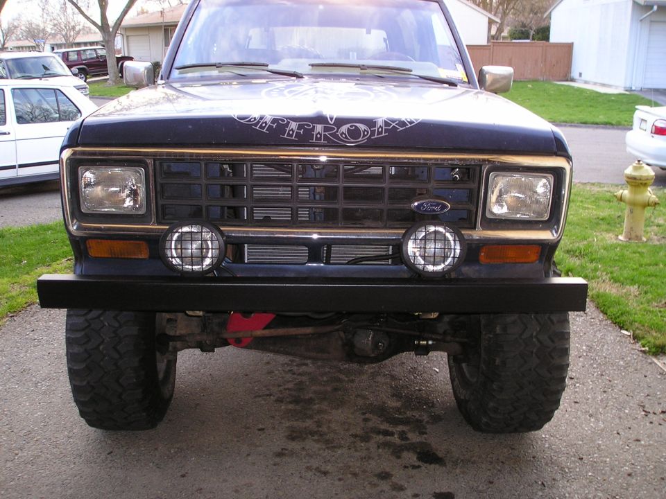 Dark blue lifted Ford SUV with homemade black front bumper and two round driving lights