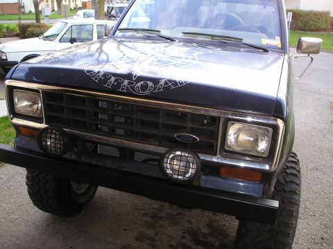 1986 Ford Bronco II - Front view of a dark blue 1986 Ford Bronco II with off-road lights and a custom decal on the hood.
