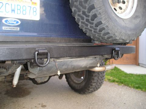 1986 Ford Bronco II - The rear of a blue SUV shows a black bumper with tow hooks and a spare tire mounted above.