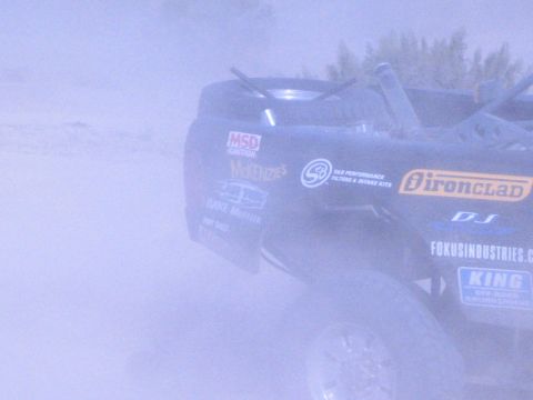 Rear of dark off-road race truck covered in sponsor decals in heavy dust
