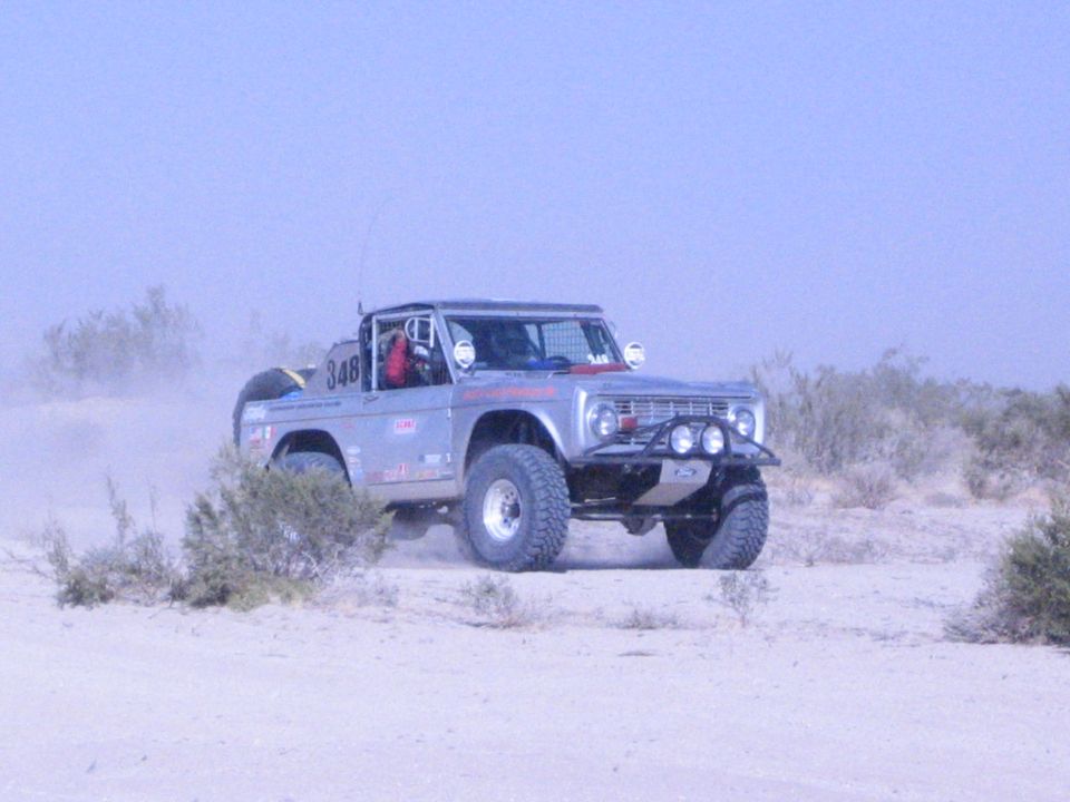 Silver off-road race truck number 348 with triple lights jumping in desert