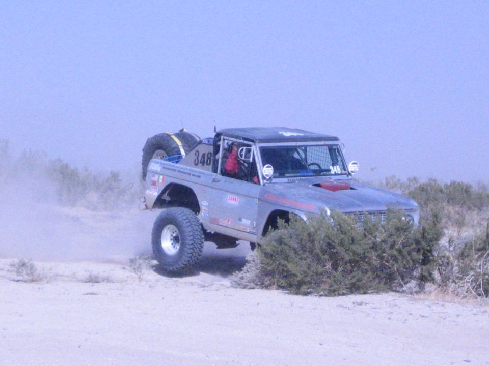 Silver number 348 off-road race truck with spare tire, front wheels airborne