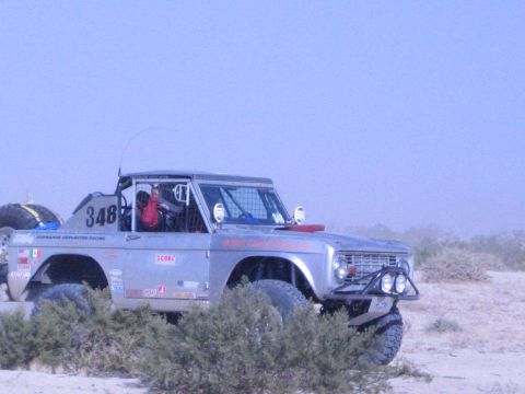 Silver number 348 race truck with Mexican flag decal parked among desert brush