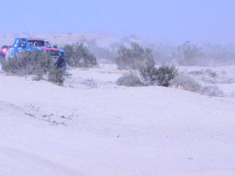 Red, white and blue off-road race truck cresting a sandy dune in the desert