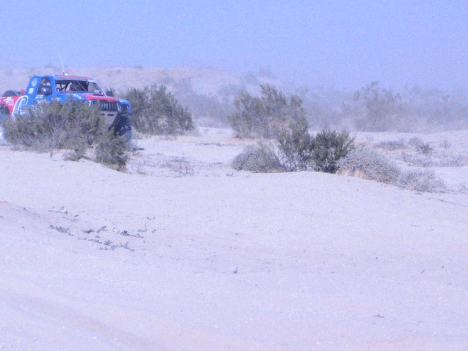 Red, white and blue off-road race truck cresting a sandy dune in the desert