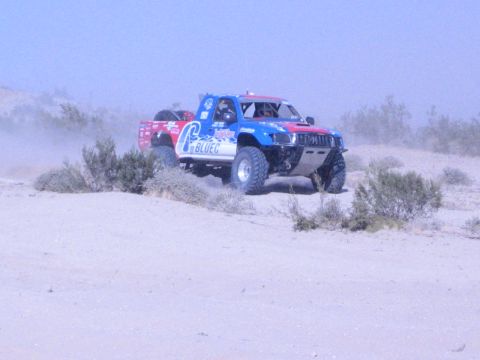 Red, white and blue Blue C off-road race truck driving over desert brush