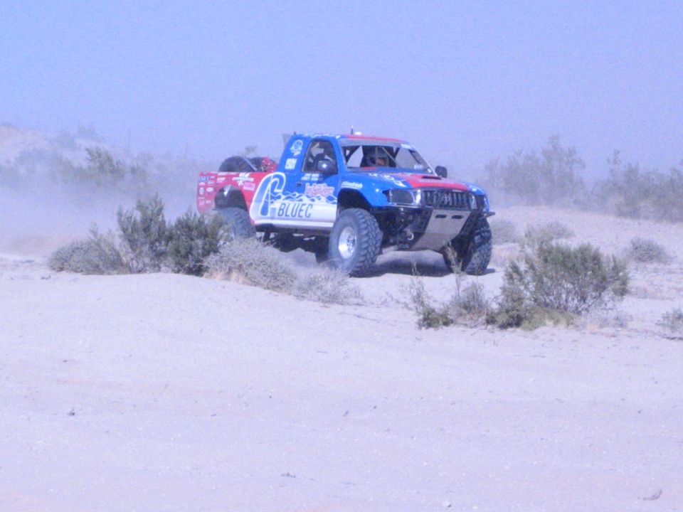 Red, white and blue Blue C off-road race truck driving over desert brush