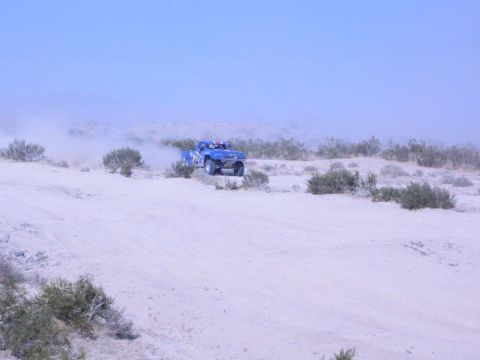 Blue off-road race truck in the distance trailing dust across desert flat