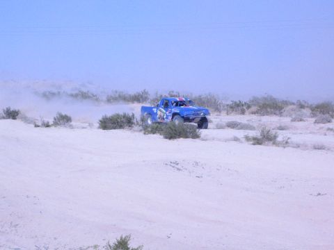 Blue off-road race truck on big tires crossing pale desert sand