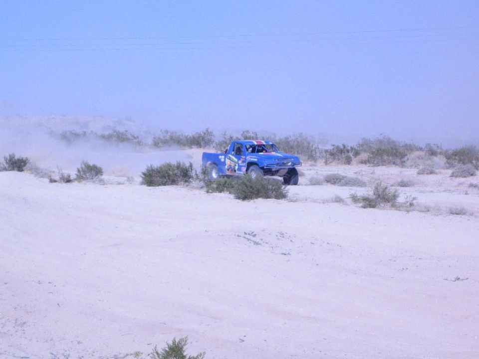 Blue off-road race truck on big tires crossing pale desert sand