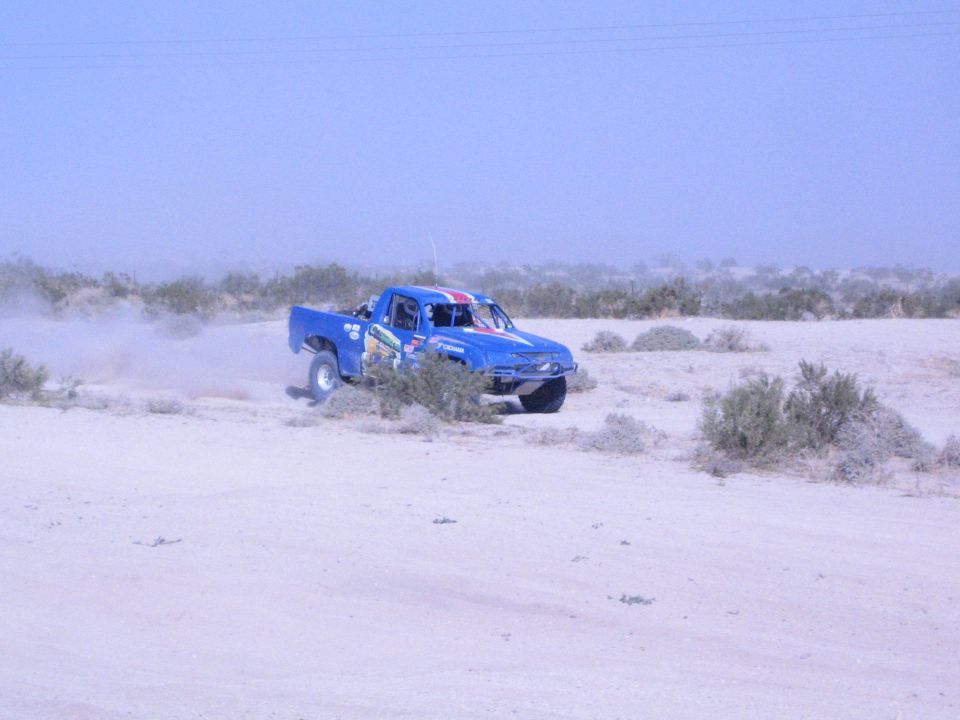 Blue off-road race truck turning on a sandy desert flat kicking up dust