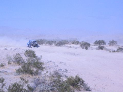 Off-road race truck far in the distance amid heavy dust on desert flat