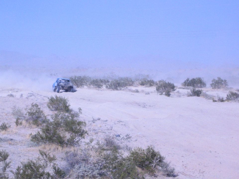 Off-road race truck far in the distance amid heavy dust on desert flat