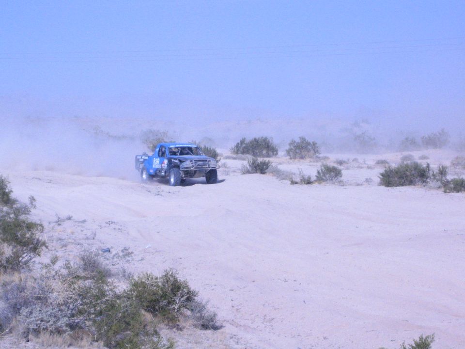 Blue off-road race truck cresting a sandy rise on a desert course