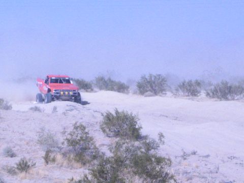 Red off-road race truck on a sandy desert berm with brush in foreground