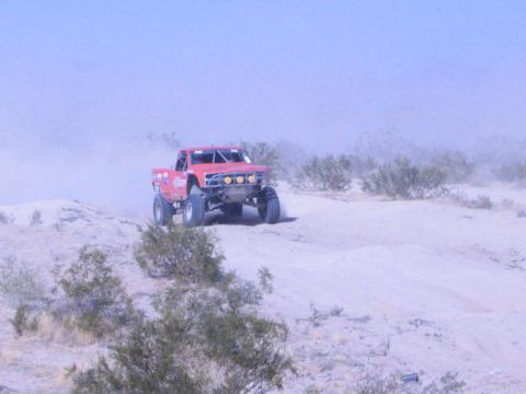 Red off-road race truck on a sand dune with desert brush and haze