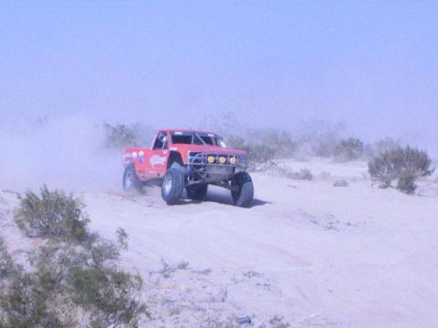 Red race truck with sponsor decals racing across desert sand throwing dust