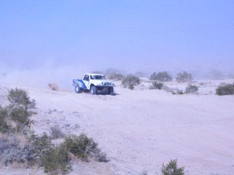 White and blue off-road race truck on pale desert sand with dust cloud