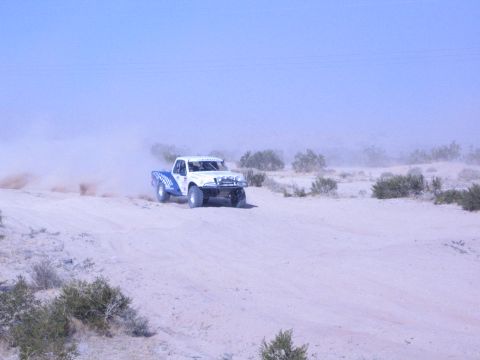 White and blue race truck throwing up a large dust plume on desert sand