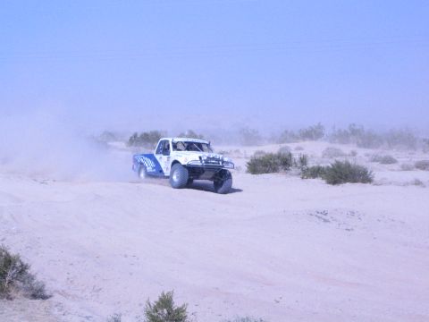 White and blue off-road race truck turning on sandy desert track