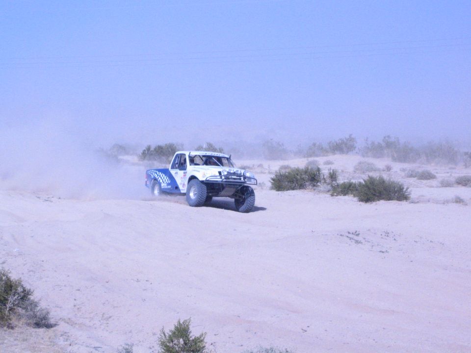 White and blue off-road race truck turning on sandy desert track