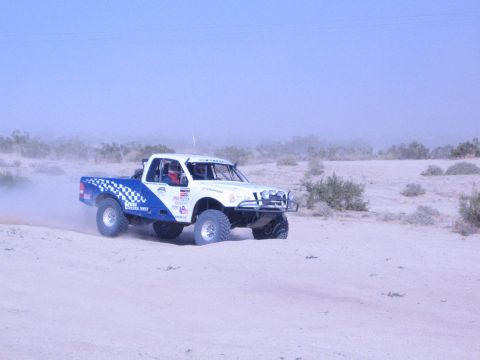 White and blue race truck with sponsor stickers on desert sand berm