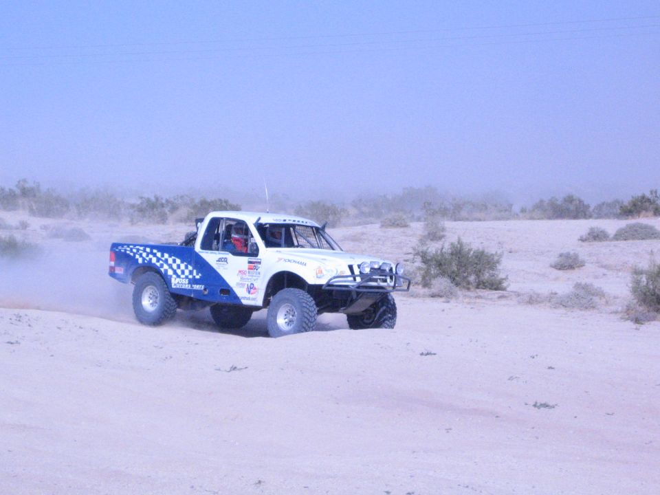 White and blue race truck with sponsor stickers on desert sand berm