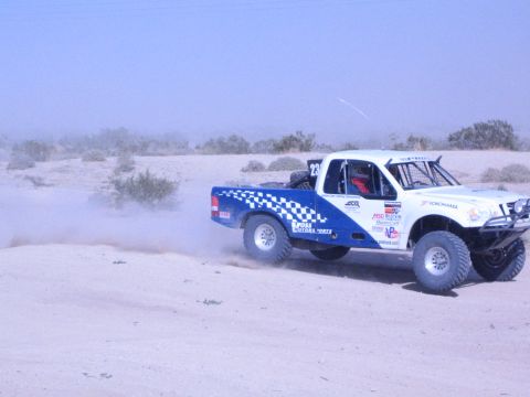 White and blue checkered pickup race truck on desert sand in profile