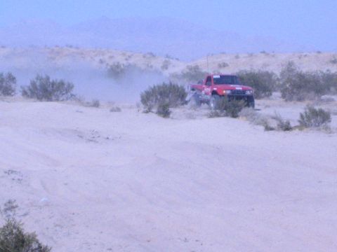 Distant red off-road truck on a sandy desert hill with mountains beyond