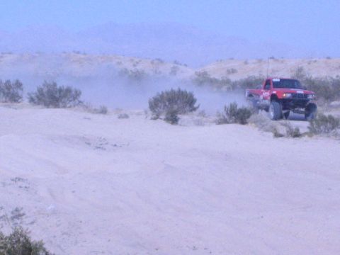 Red off-road race truck with antenna on a desert ridge against mountains