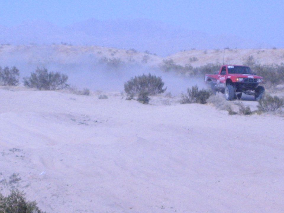 Red off-road race truck with antenna on a desert ridge against mountains