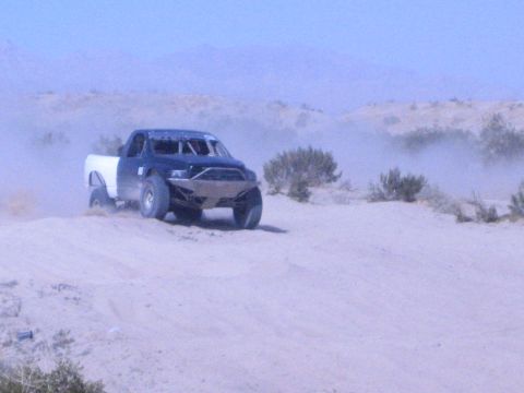 Dark blue tube-frame race truck with white bed cresting a desert berm