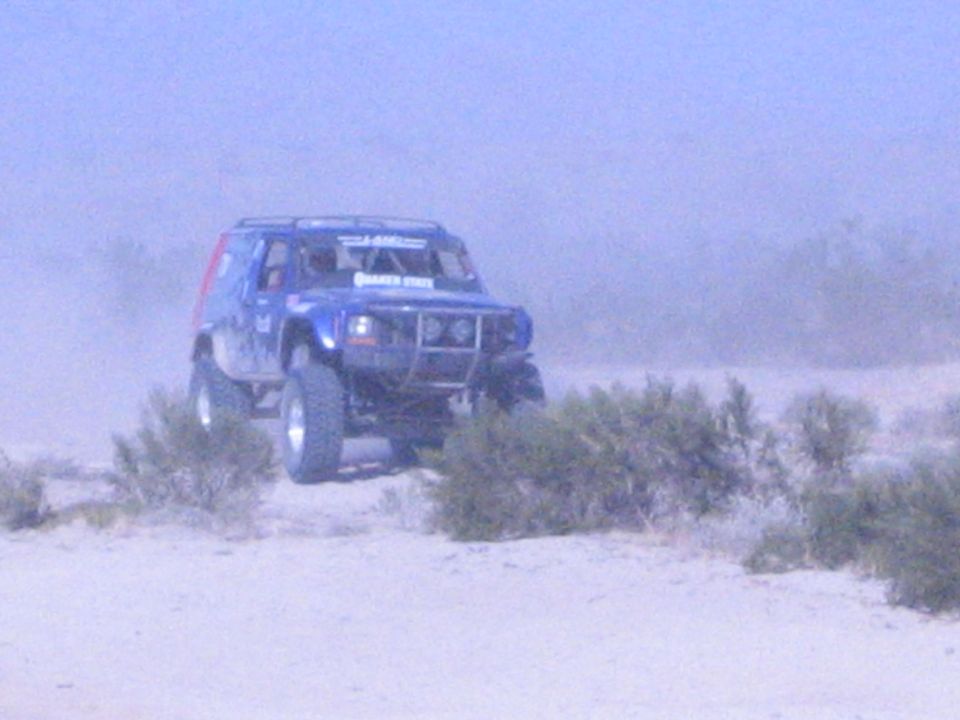 Blue off-road SUV race vehicle with roof rack on hazy desert sand