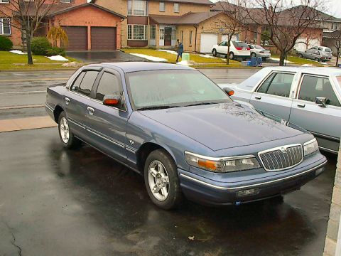 1985 Mercury Grand Marquis - Blue sedan parked in a driveway with houses in the background.